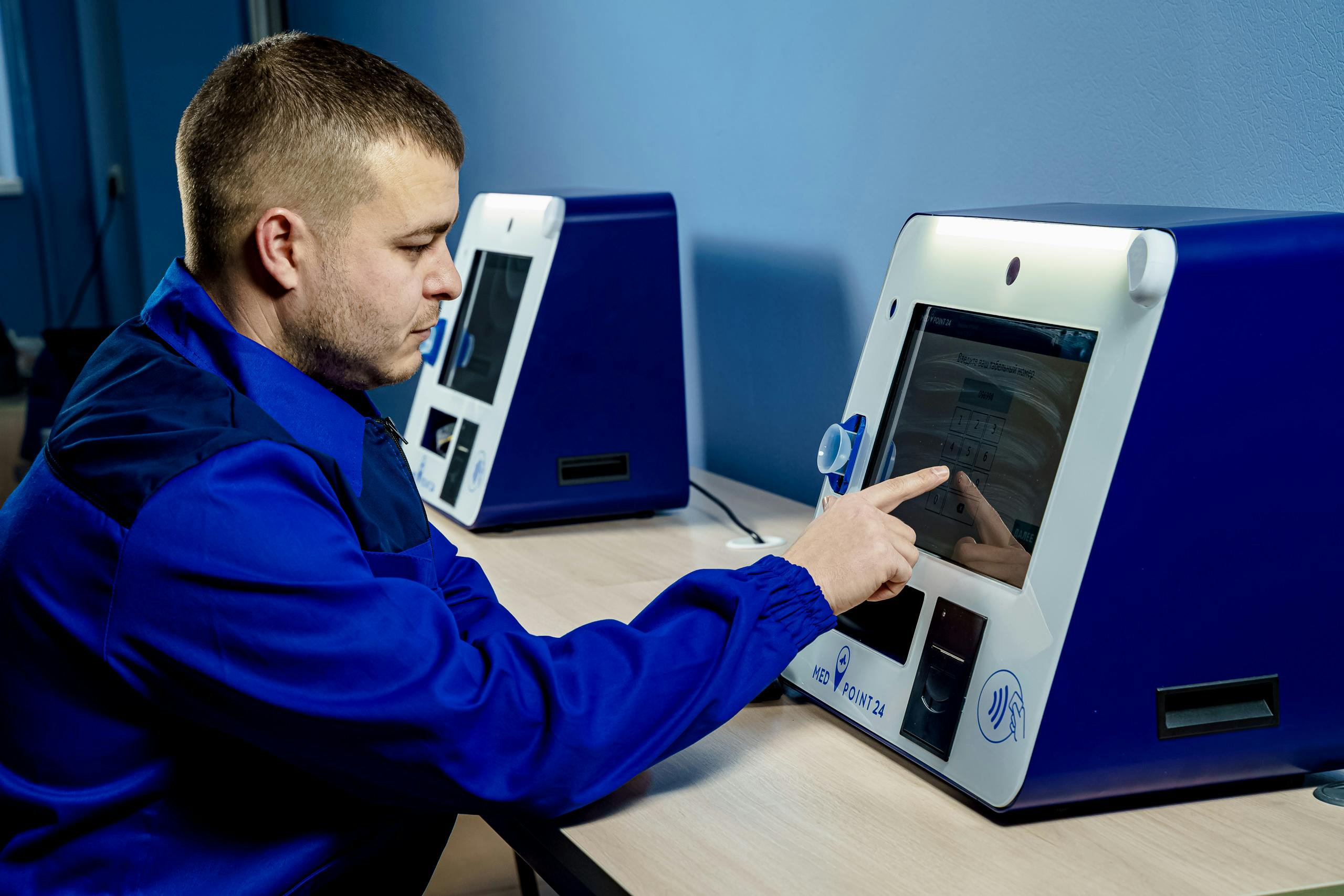 Adult male engineer interacts with a smart touchscreen vending machine in an industrial setting.