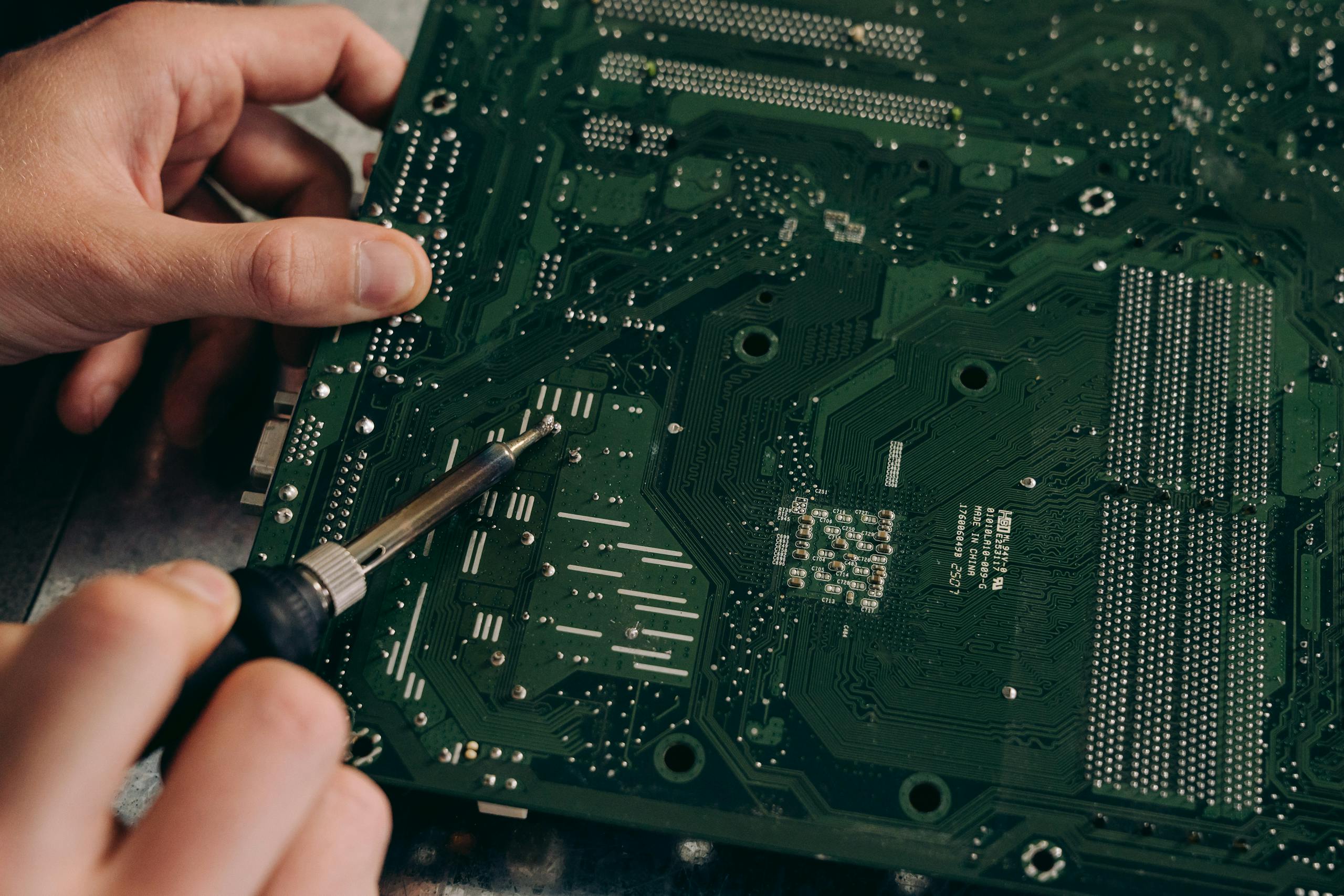 Hands soldering a motherboard with precision demonstrating electronics repair skills.