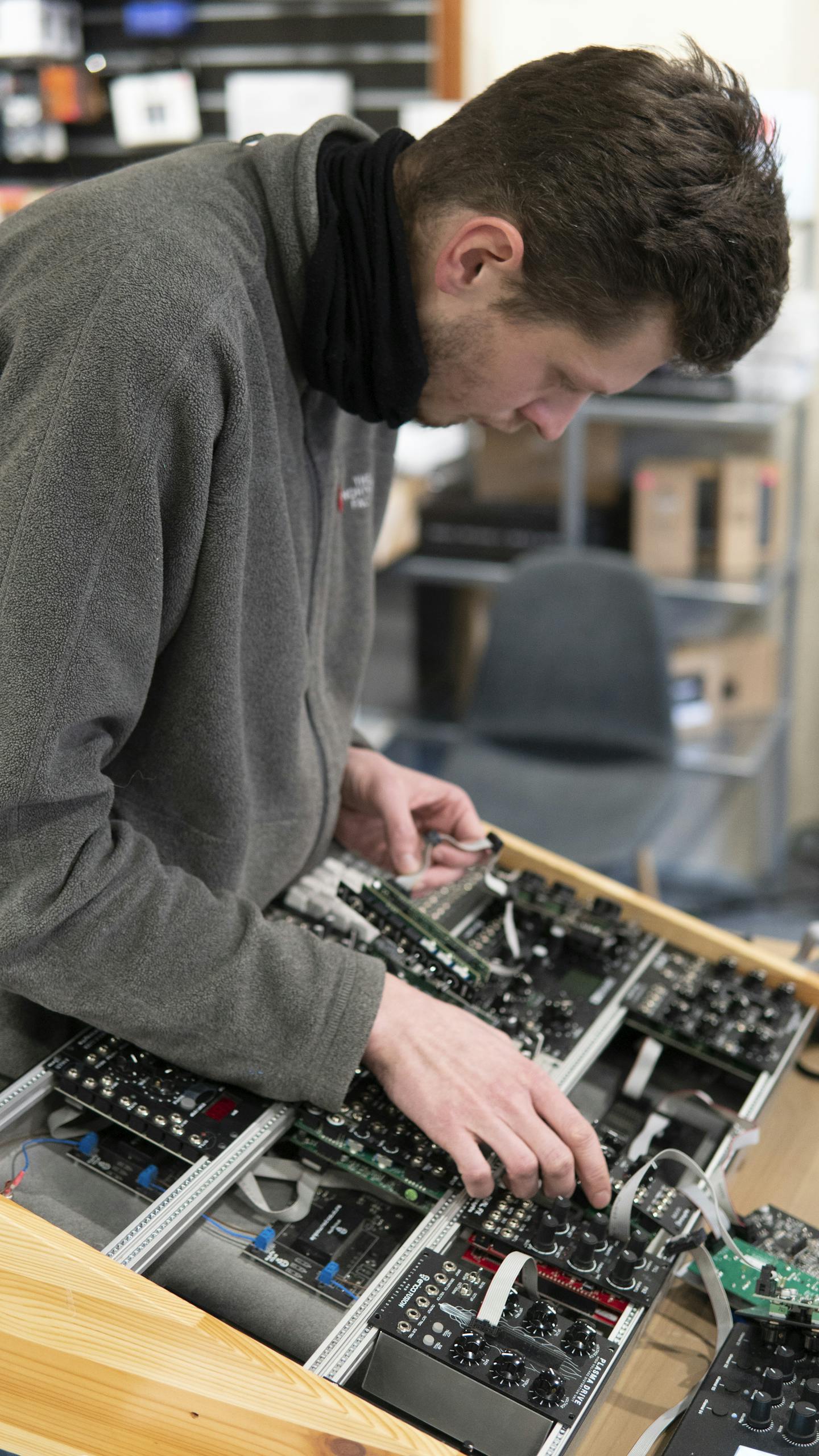 Man in a gray sweater assembling modular synthesizer in a recording studio.
