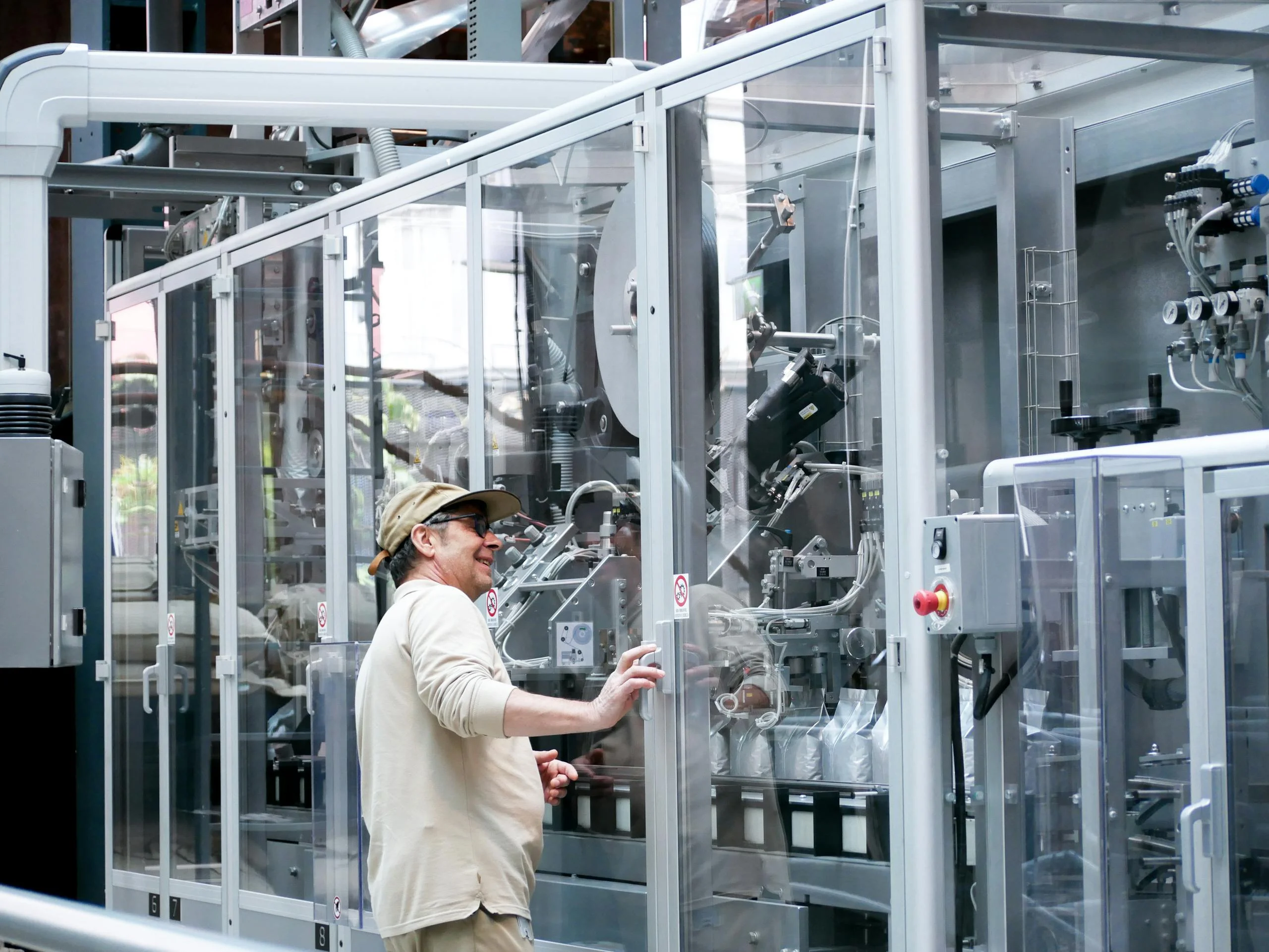 Man observes and operates advanced industrial machinery behind glass indoors.